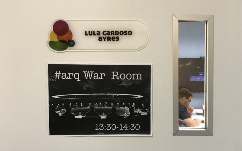 #PraCegoVer porta da sala Lula Cardoso Ayres com um cartaz colado identificando que das 13:30 às 14:30 esta é a #arq War Room